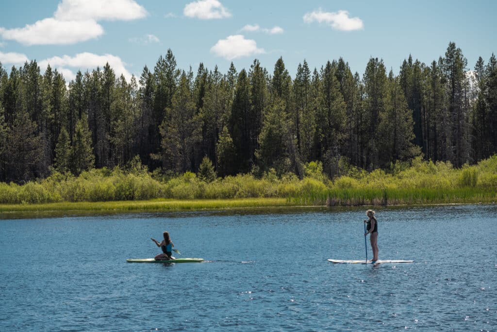 Two girls paddleboarding on Gilchrist Log Pond at the Historic Gilchrist Waterfront Resort.